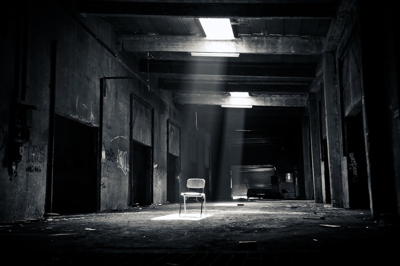 brand-02 A haunting black and white photo of an abandoned warehouse with a solitary chair illuminated by sunlight through a window.
