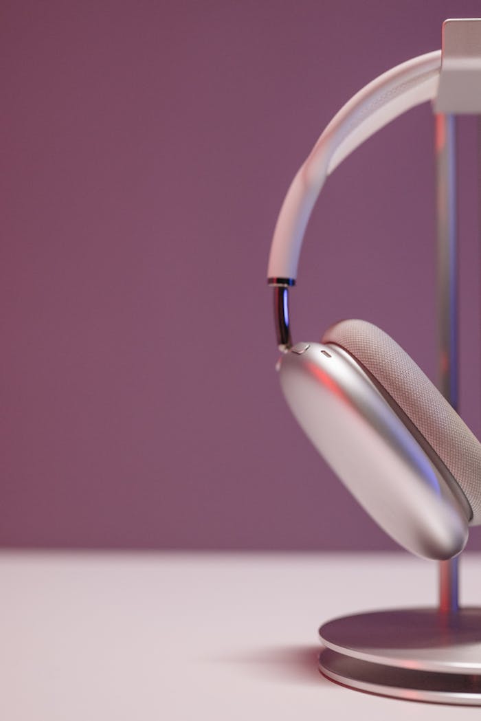 mobile-01 Close-up of sleek silver over-ear headphones on a stand against a purple backdrop.